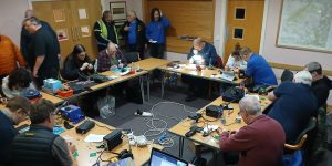 Group of people sat around tables working on amateur radio construction activities