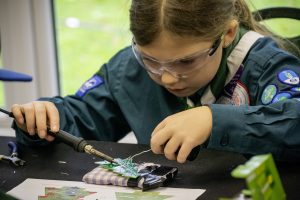 Young girl in Scout uniform wearing safety goggles whilst soldering