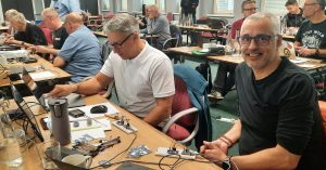 Group of radio amateur sat behind rows of desks taking part in hands-on programming workshop